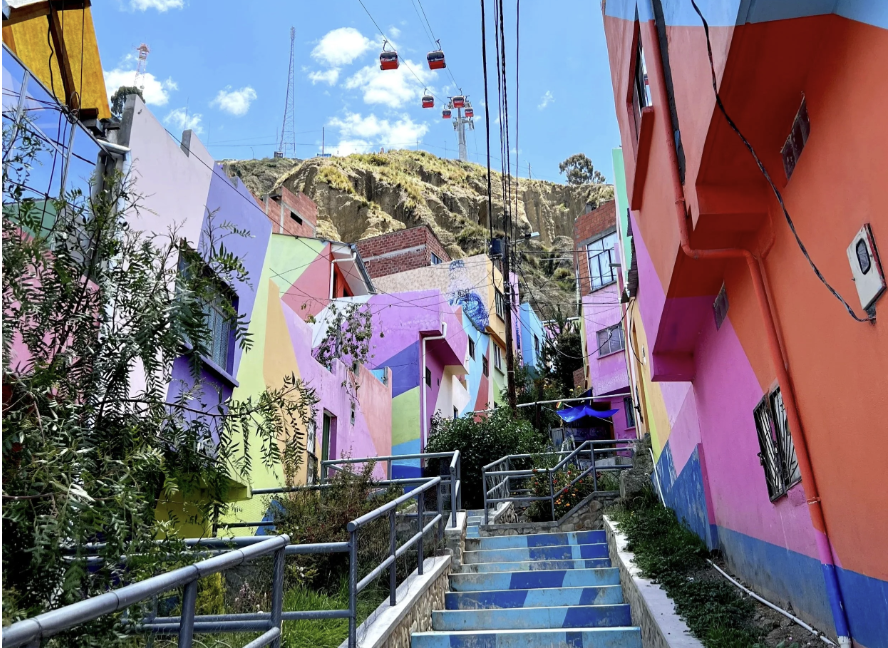 Brightly painted houses on a steep La Paz hillside with red cable cars passing overhead