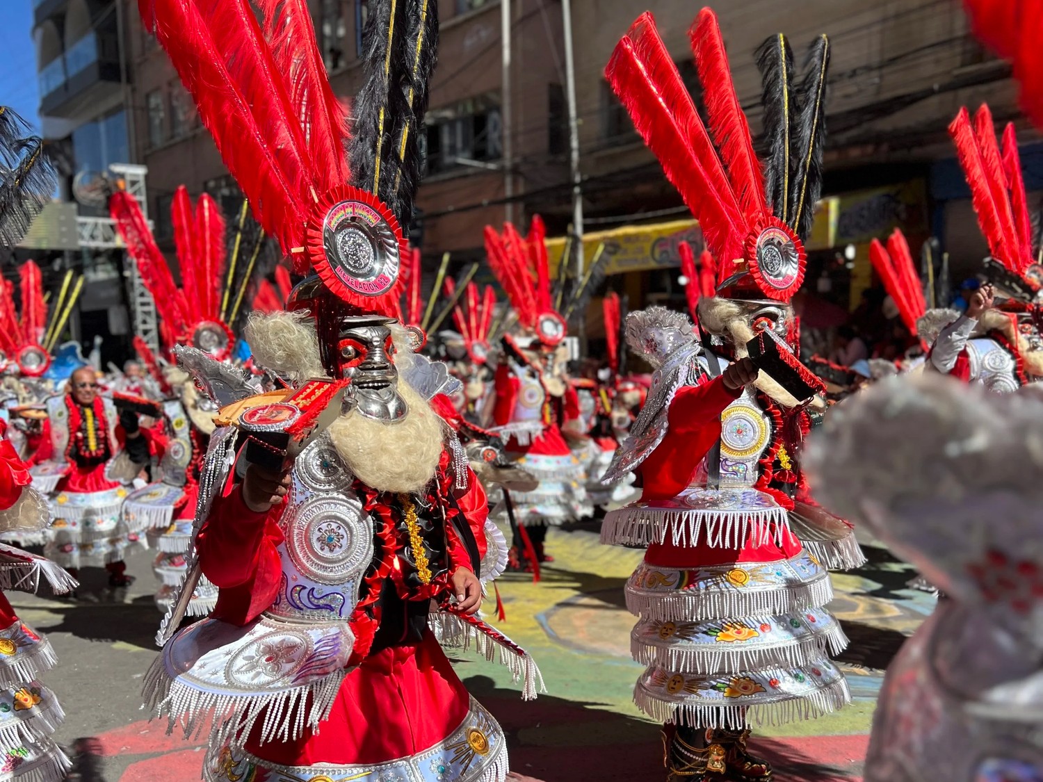 Morenada dancers in red feathered headdresses marching down a La Paz street
