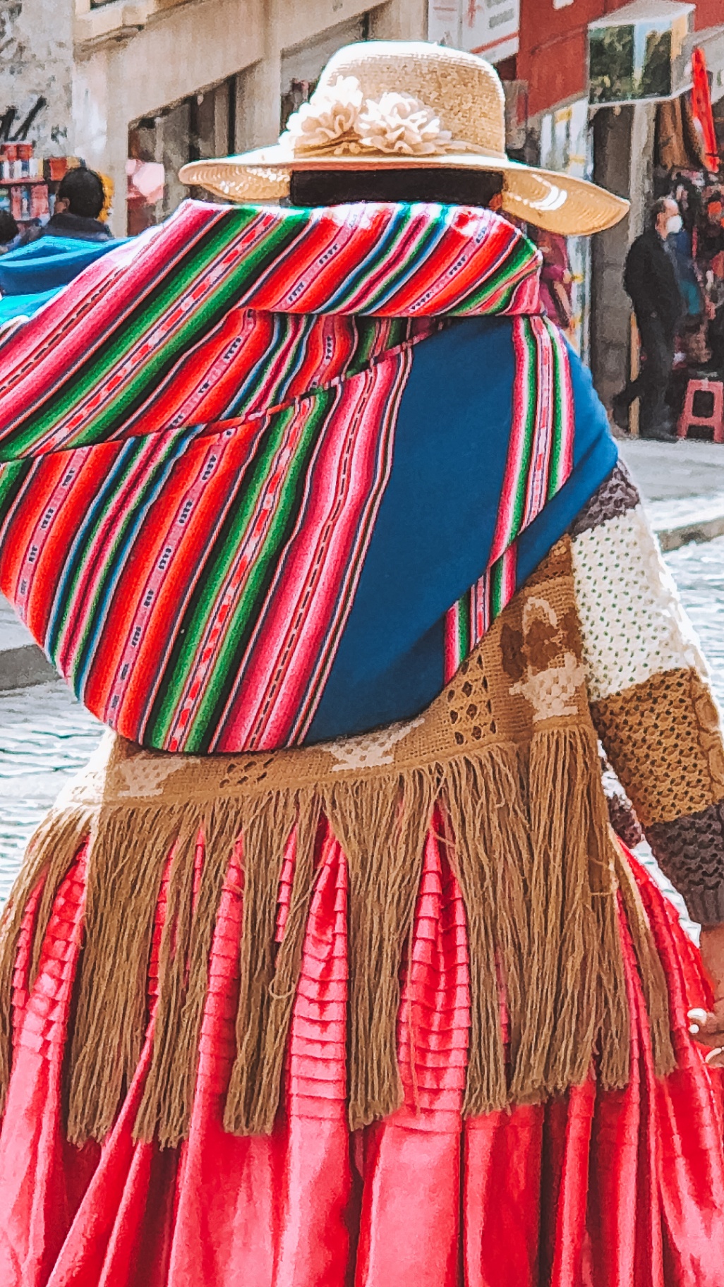 Cholita paceña in traditional dress with a striped aguayo walking through La Paz