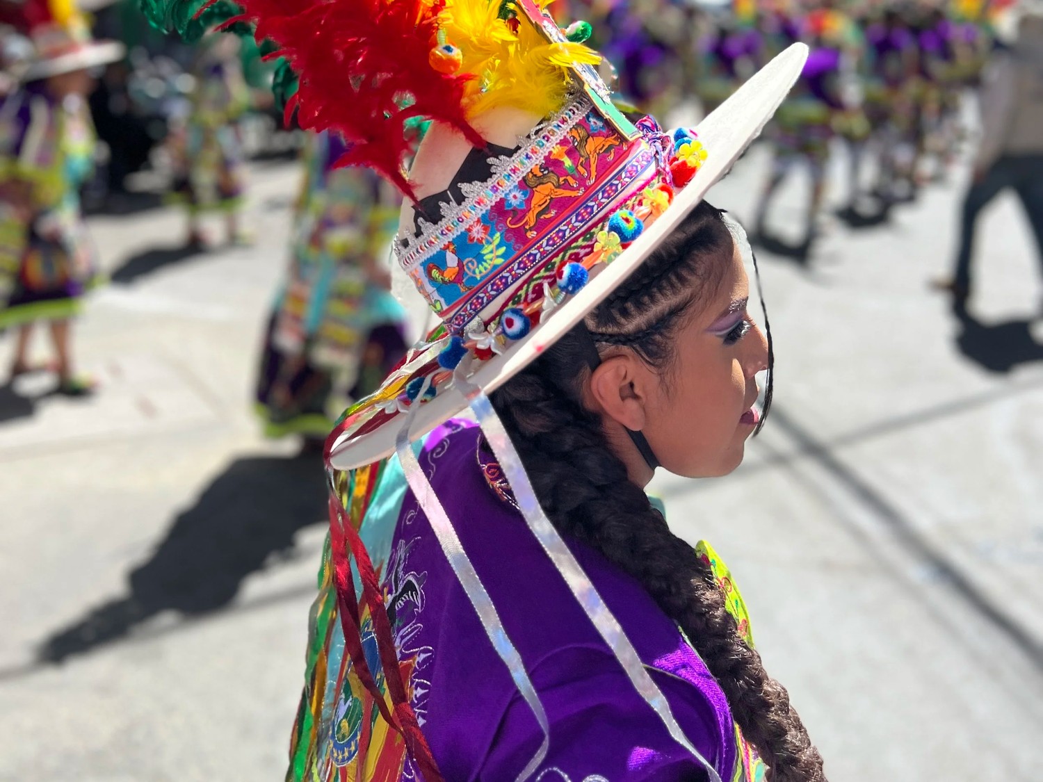 A young dancer in a colorful hat and purple costume, seen in profile during the parade